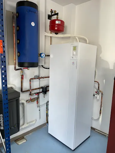 Module intérieur Atlantic dans un local technique, avec un ballon tampon bleu et un vase d'expansion rouge au mur