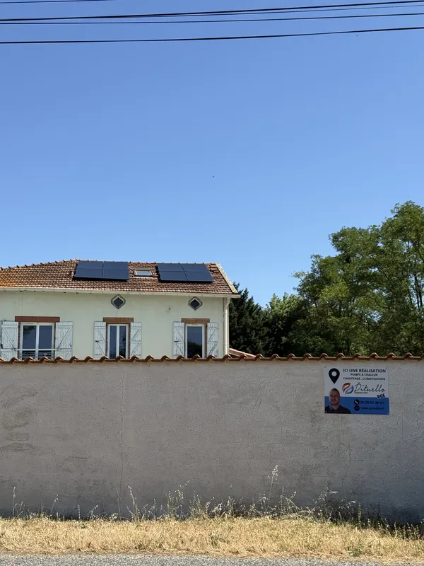 Maison de Calmont vue derrière son mur de clôture, panneaux photovoltaïques sur le toit et panneau « Ici une réalisation Pituello » sur le mur
