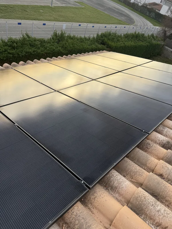 Gros plan sur des panneaux photovoltaïques noirs posés sur des tuiles canal à Vernet, avec la piste du stade en arrière-plan, janvier 2026