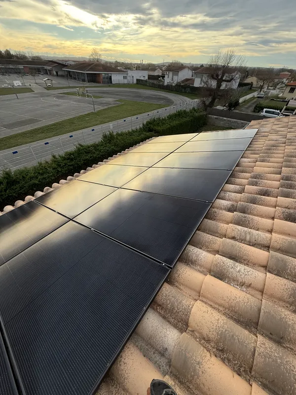 Toiture en tuiles canal à Vernet avec ses panneaux photovoltaïques noirs, vue sur le stade, sa piste et les mâts d'éclairage, janvier 2026